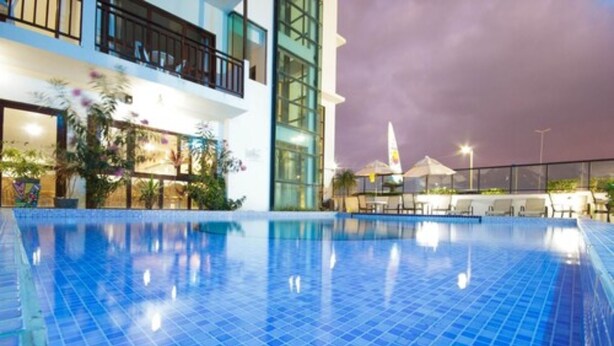 A swimming pool with blue tiles, surrounded by a building with balconies and glass windows. - Pousada dos Jangadeiros (Maragogi)