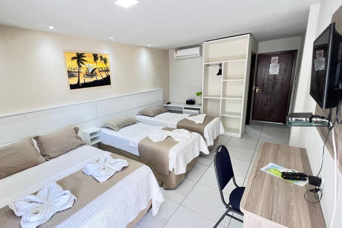Ein Hotelzimmer mit drei Betten, einem Schreibtisch, einem Fernseher und einem Bild an der Wand.
