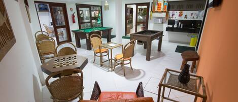 Una sala de estar con mesa de billar, mesa de fútbol de mesa y zona de comedor con sillas de mimbre.
