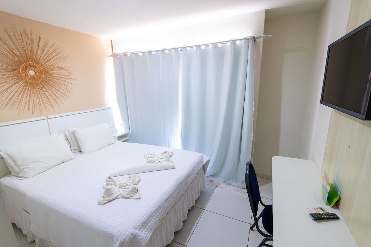 Ein Hotelzimmer mit einem Bett, einem Schreibtisch, einem Stuhl, einem Fernseher und einem Vorhang.