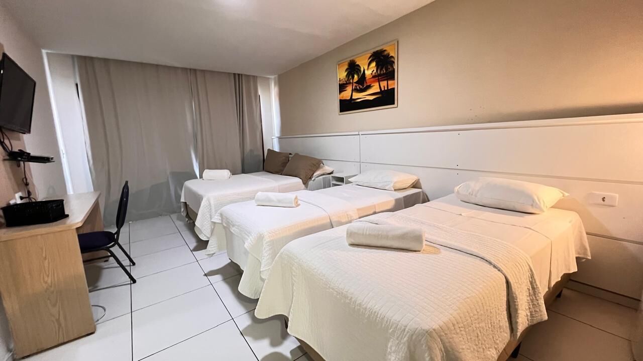 A hotel room with three beds, a desk, a chair, and a television on the wall.