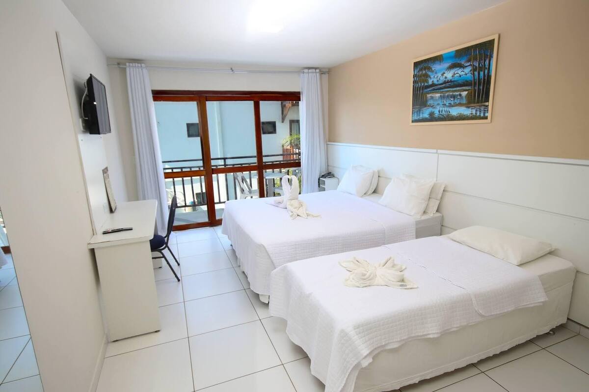 Ein Hotelzimmer mit zwei Betten, einem Schreibtisch und einem Balkon mit Blick ins Freie.