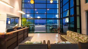A modern hotel lobby with a reception desk, wicker furniture, large windows offering a view of the sea, and hanging pendant lights. - Pousada dos Jangadeiros (Maragogi)