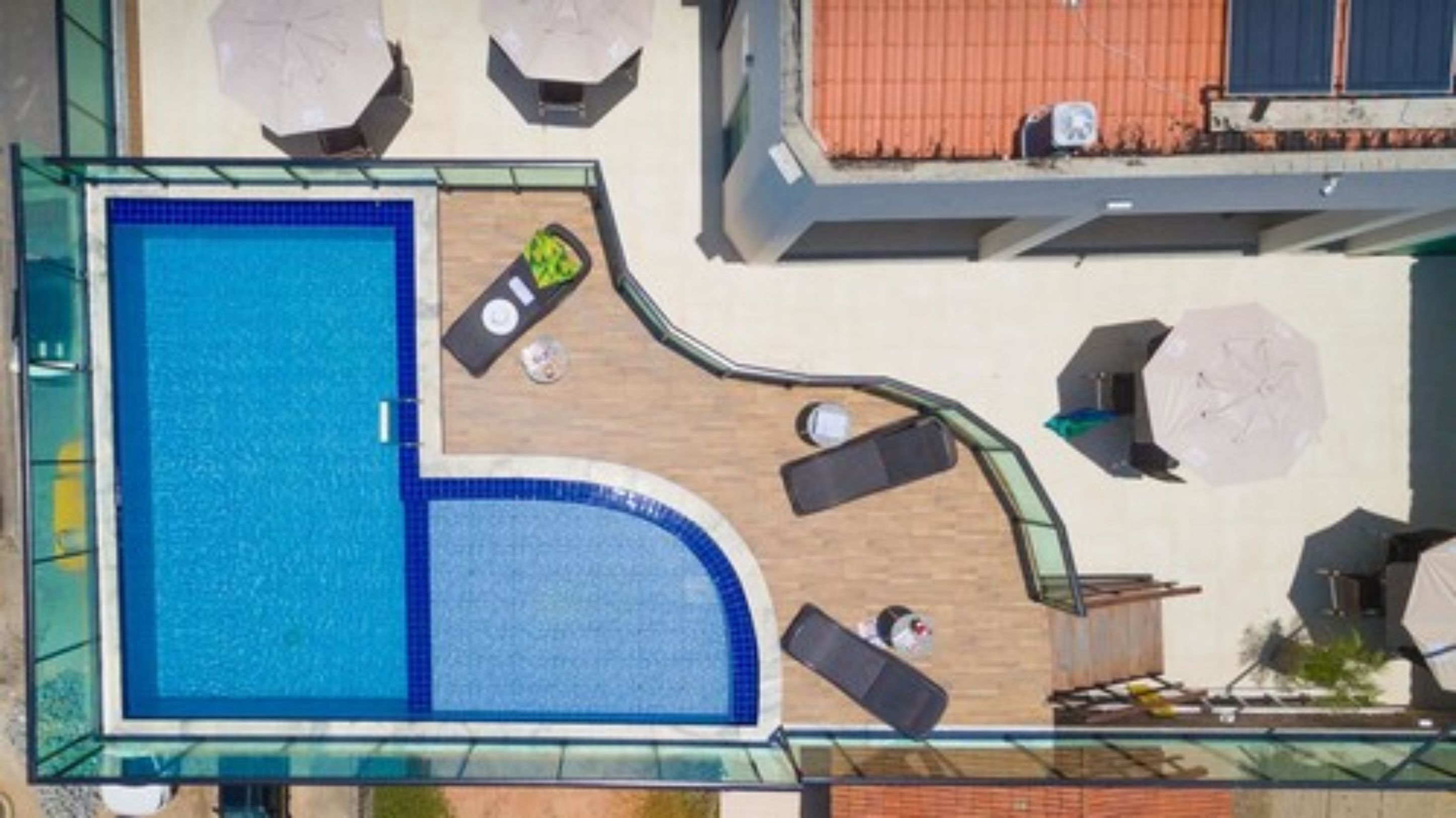 An aerial view of a rooftop swimming pool with sun loungers and a small deck area.