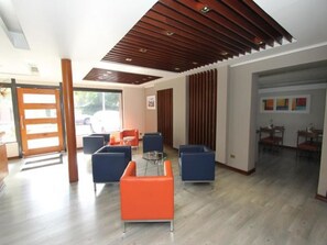 A modern lobby with a wooden ceiling, blue and orange seating, and a glass partition. - Hotel El Vergel (Santiago)