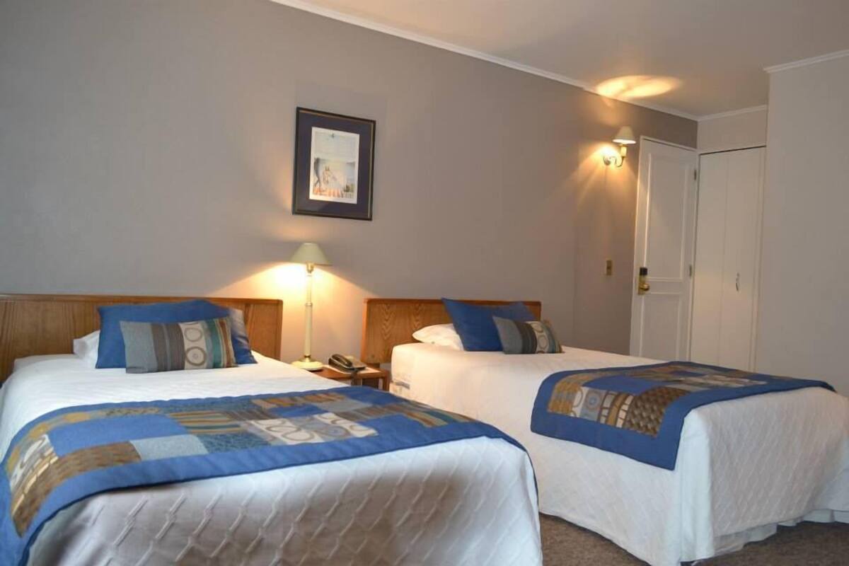 A hotel room with two beds, each with a blue and white quilt, a bedside lamp, and a framed picture on the wall.