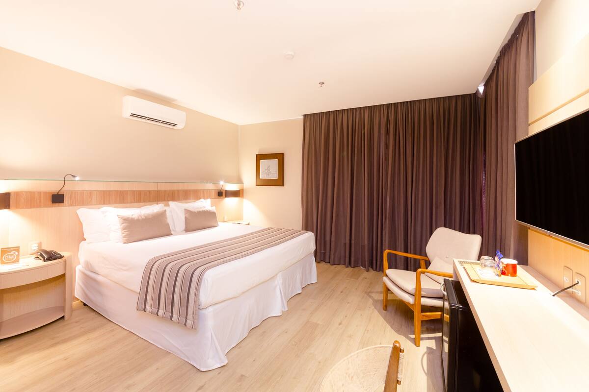 A hotel room with a bed, bedside table, lamp, chair, desk, and a large flat-screen TV.