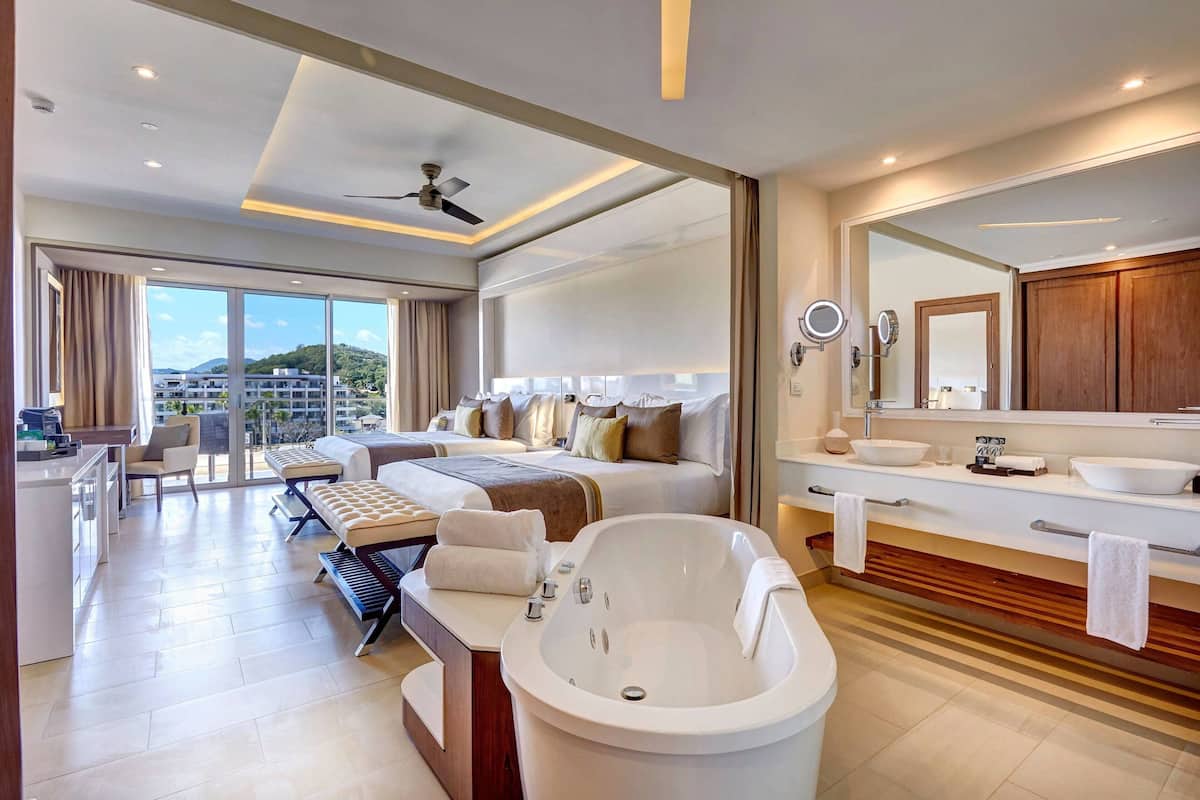 Ein modernes Hotelzimmer mit einem großen Bett, einer Sitzecke, einer Badewanne und einem Balkon mit Blick auf die Stadt.