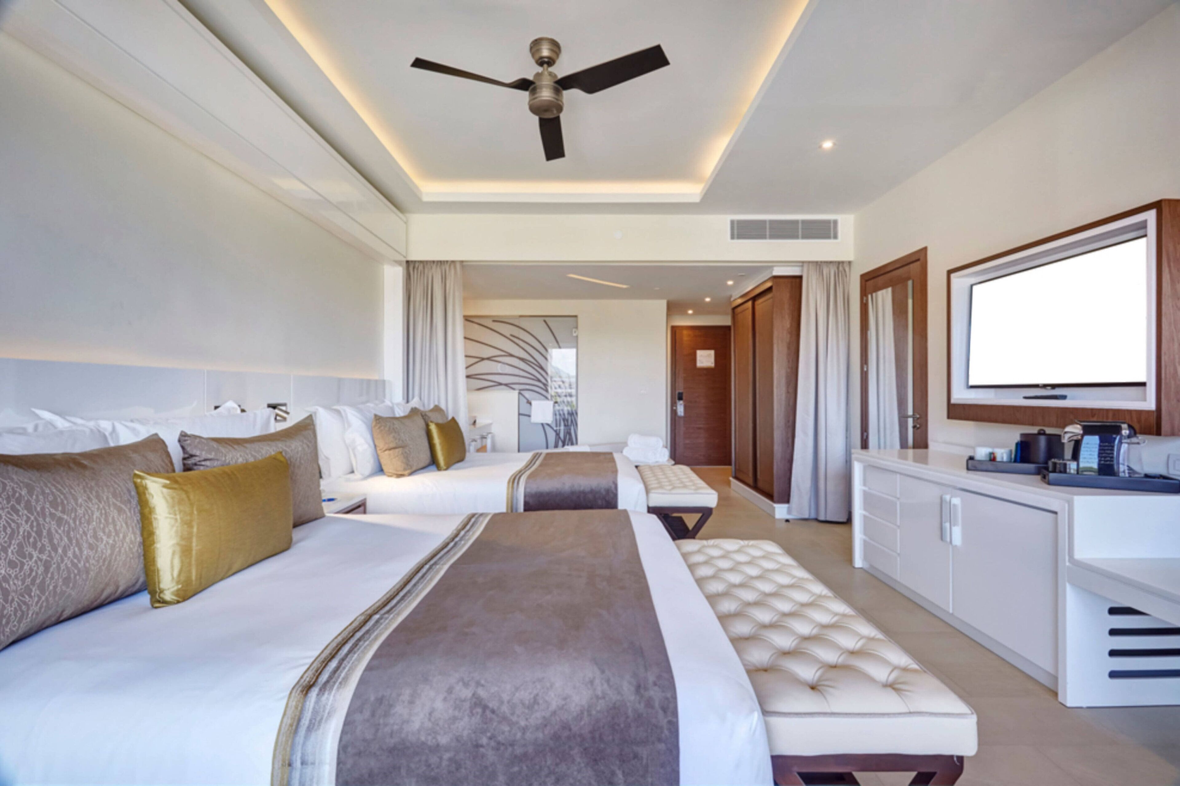 A modern hotel room with two beds, a sofa, a TV, and a kitchenette.