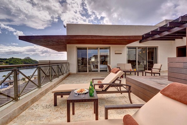Un balcon agrémenté de meubles en osier, une table avec une bouteille et une assiette, et une vue sur la mer.