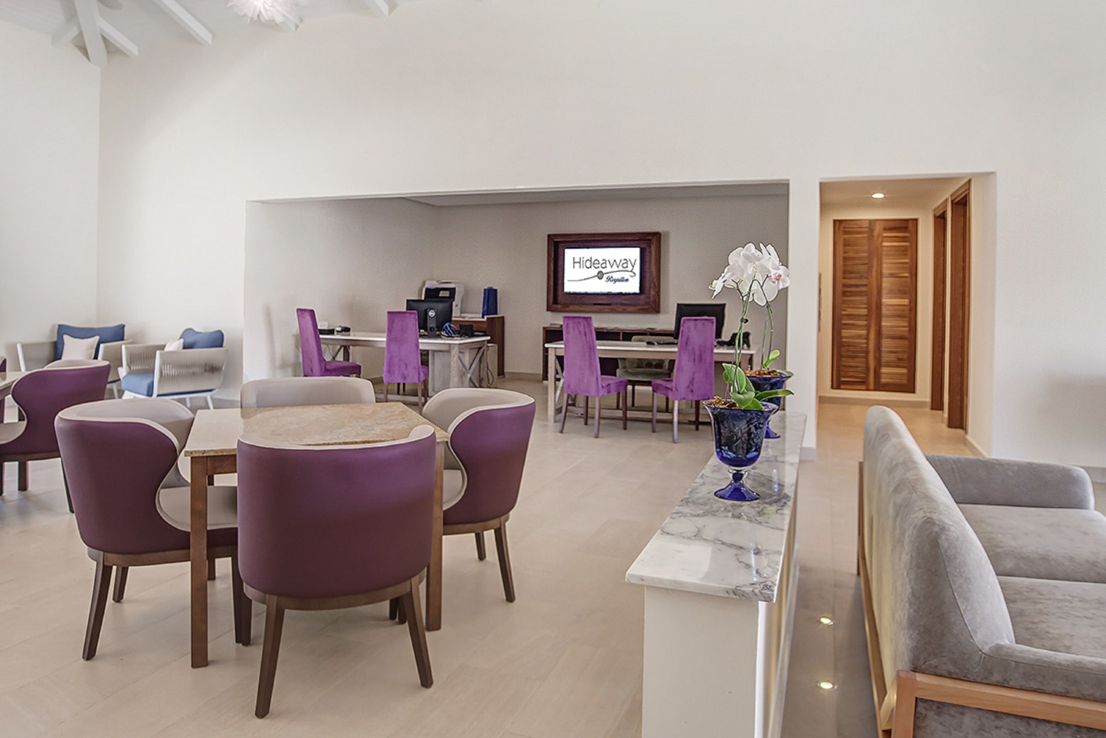 Un moderno vestíbulo de hotel con sillas moradas, un mostrador de recepción de mármol y un letrero que dice 'Hideaway Signature'.