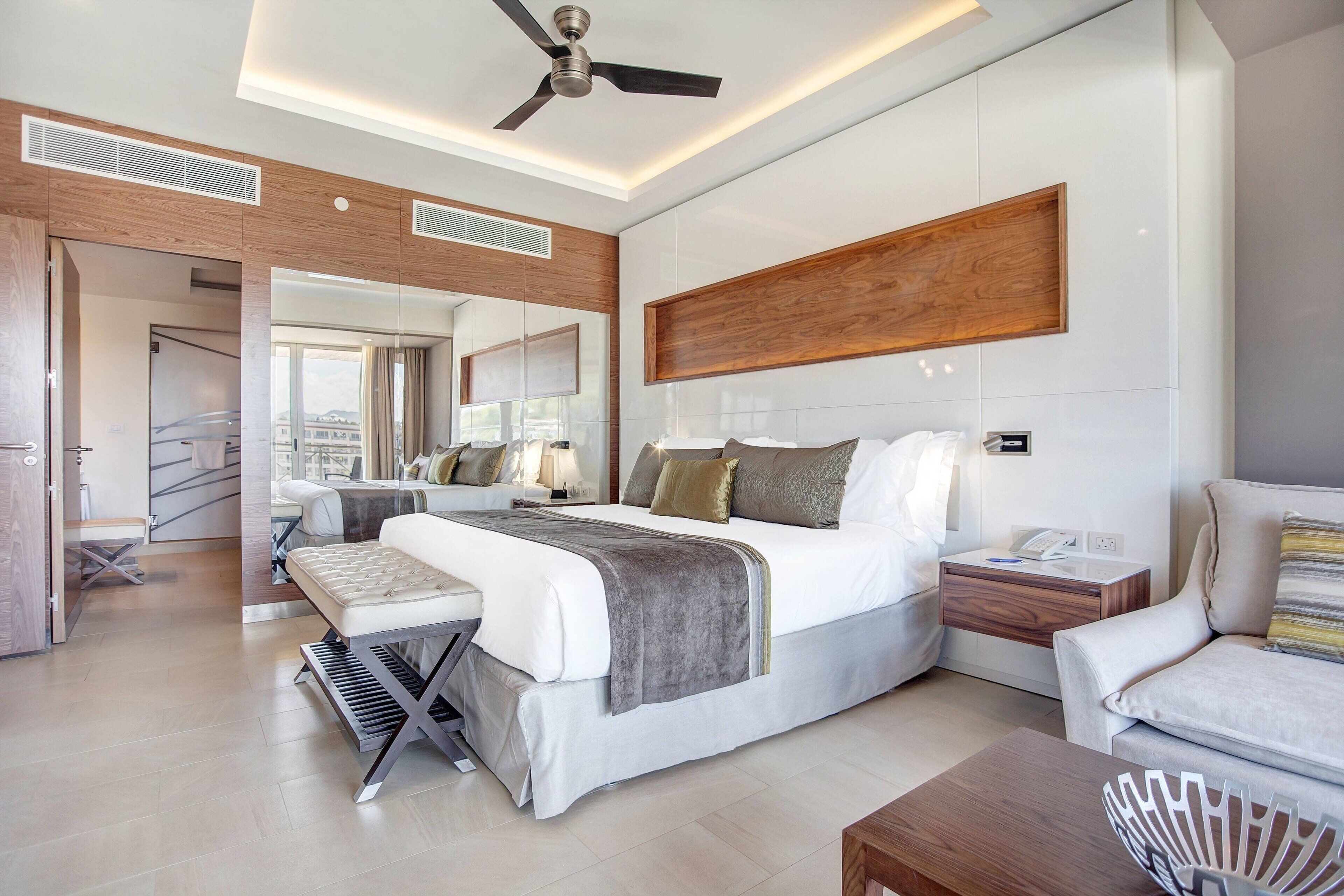 Une chambre d’hôtel moderne dotée d’un grand lit, de tables de chevet, d’un coin salon et d’un ventilateur de plafond.