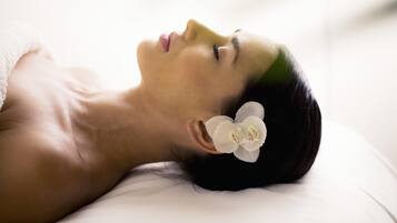 A person lying on a white surface with a white flower in their hair.