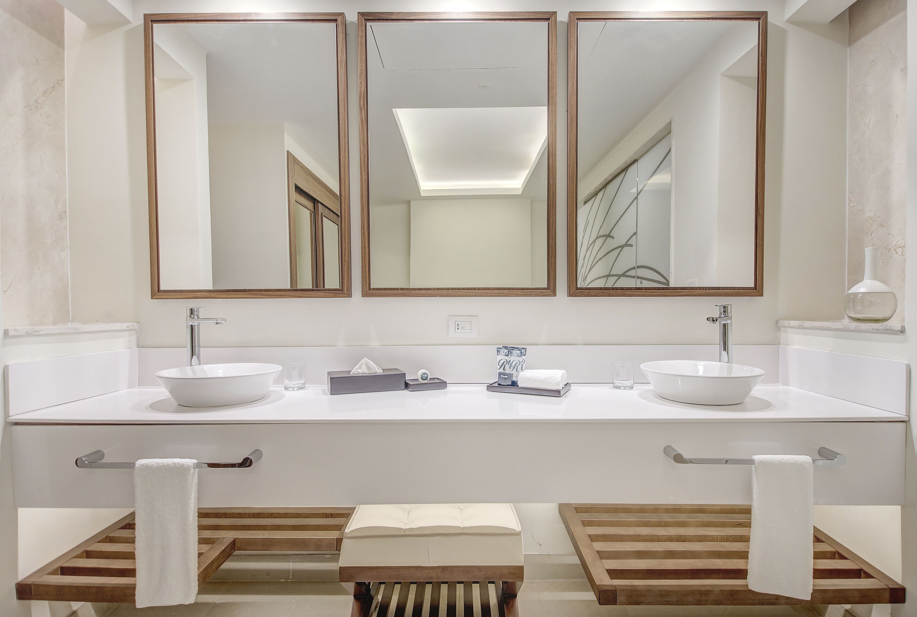 A modern bathroom with a double sink, a large mirror, and a wooden bench.