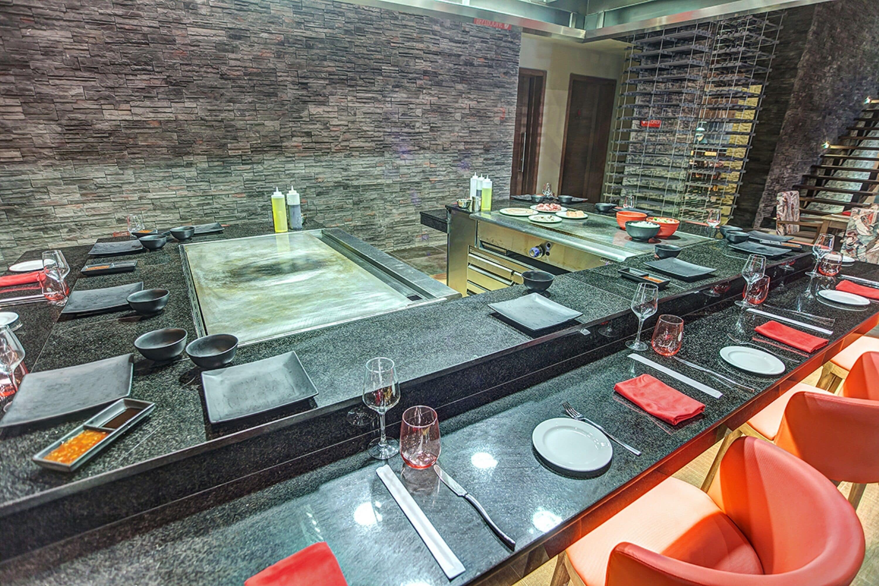 A restaurant with a long counter, multiple seating areas, and a stone wall backdrop.