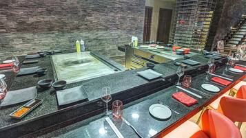 A restaurant with a long counter, multiple seating areas, and a stone wall backdrop.
