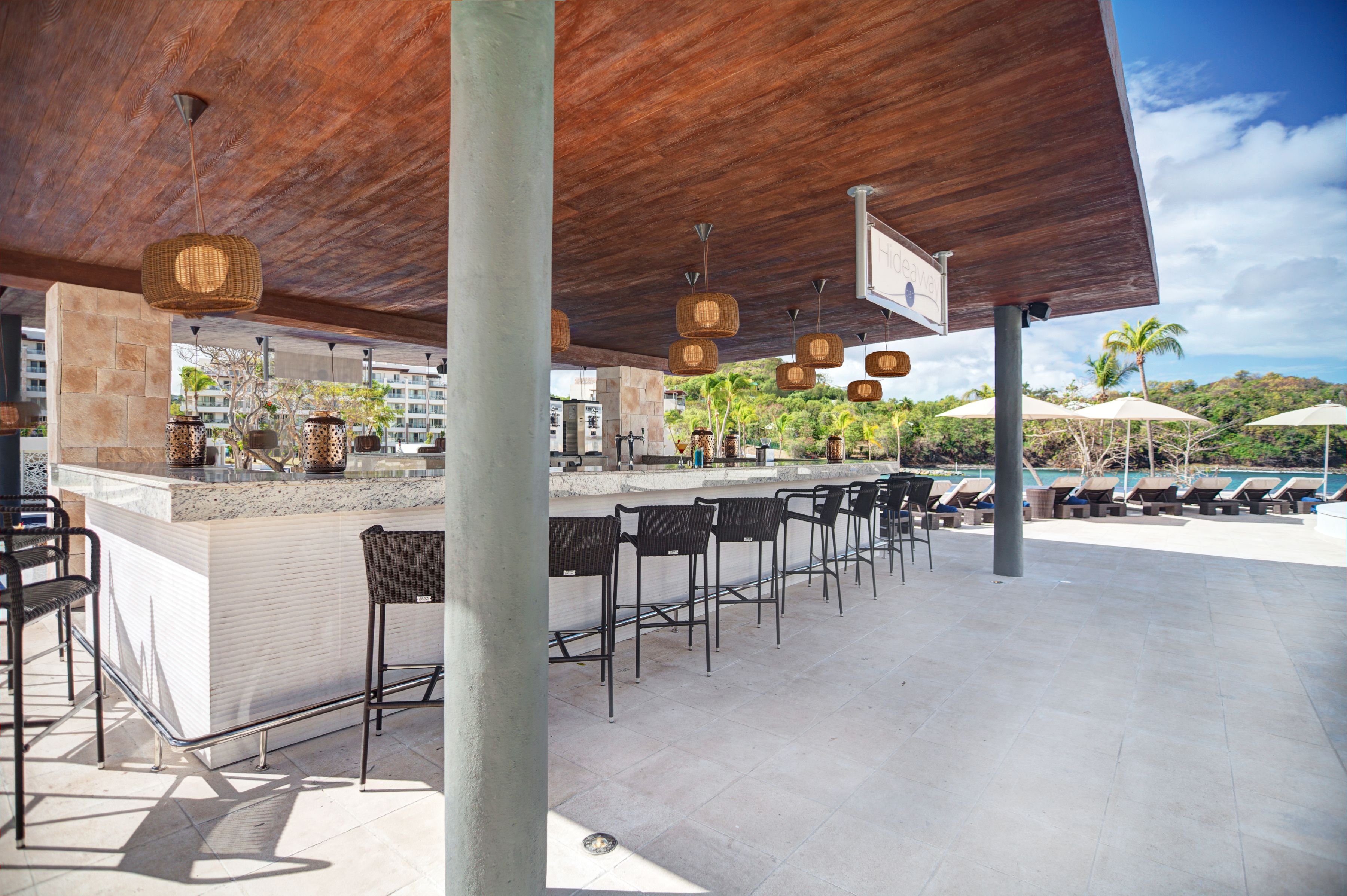An outdoor bar area with a wooden ceiling, wicker pendant lights, and a stone counter.