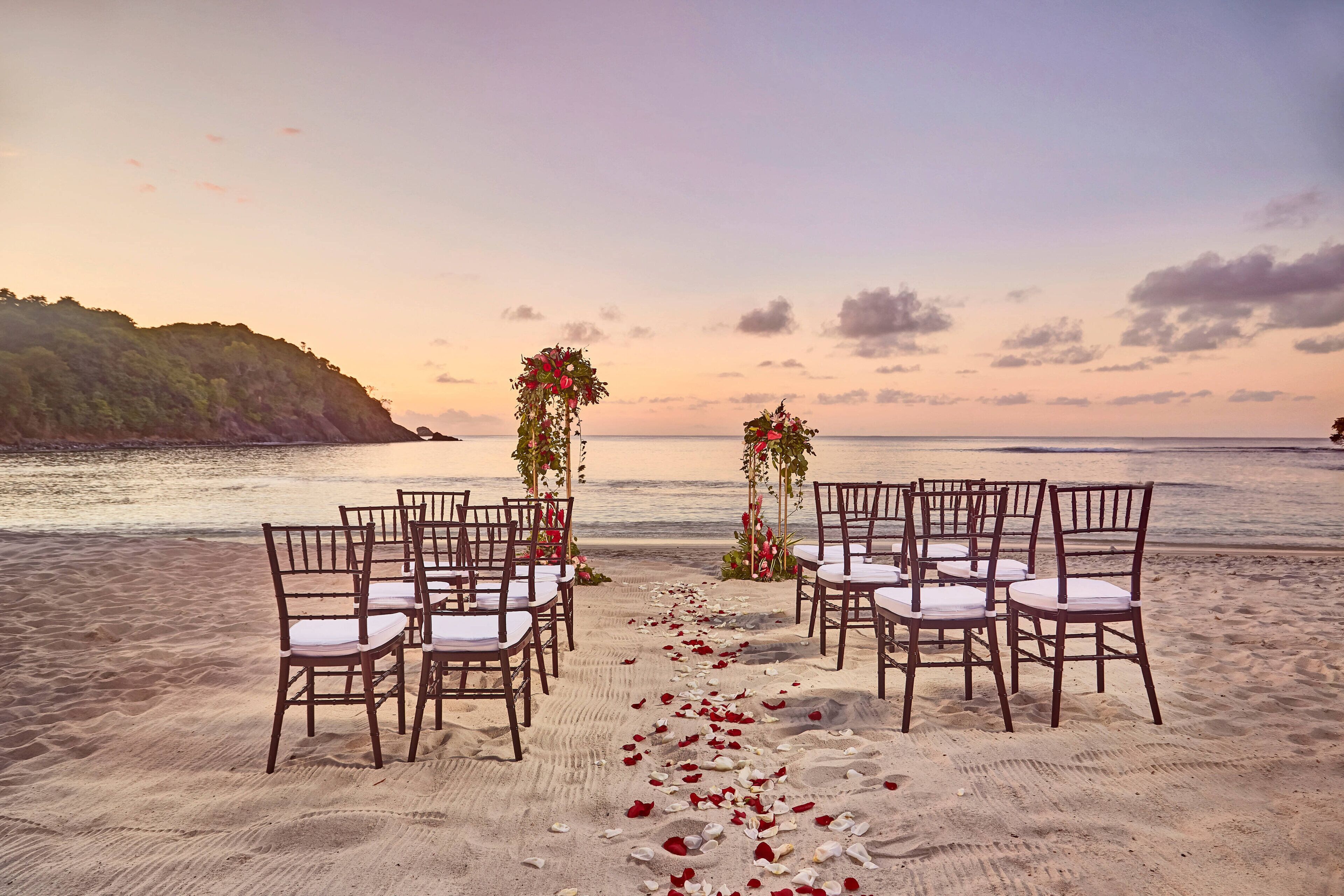 Aménagement pour un mariage sur la plage, avec des chaises et des décorations florales.