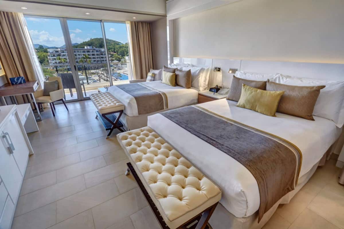 Ein Hotelzimmer mit zwei Betten, einem Schreibtisch und Blick auf eine Stadtlandschaft.