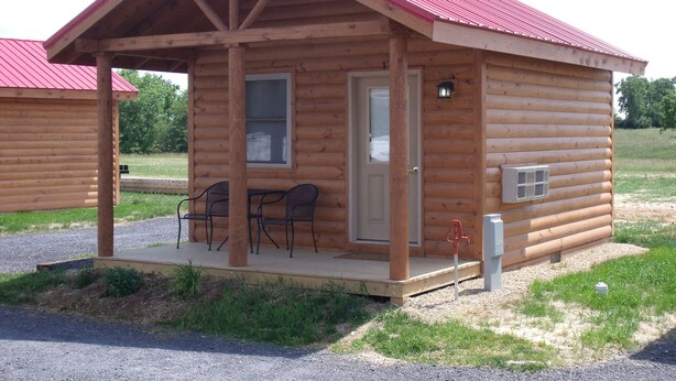 A small wooden cabin with a porch, two chairs, and a red roof. - Shenandoah Valley Campground (Quicksburg)