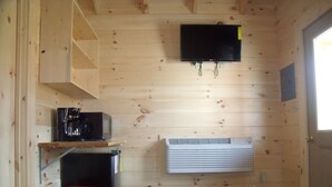 A small cabin with a wooden interior, a mounted television, a heater, a coffee maker, and a red trash bin. - Shenandoah Valley Campground (Quicksburg)