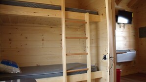 A wooden cabin room with bunk beds, a television mounted on the wall, and a heater. - Shenandoah Valley Campground (Quicksburg)