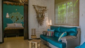 A room with a bed, a teal sofa, a small wooden stool, and a wall-mounted hanging. - Hotel Campestre Solar De La Luna (Armenia)