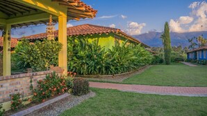 A house with a tiled roof, a covered porch, and a well-maintained garden with various plants and flowers. - Hotel Campestre Solar De La Luna (Armenia)