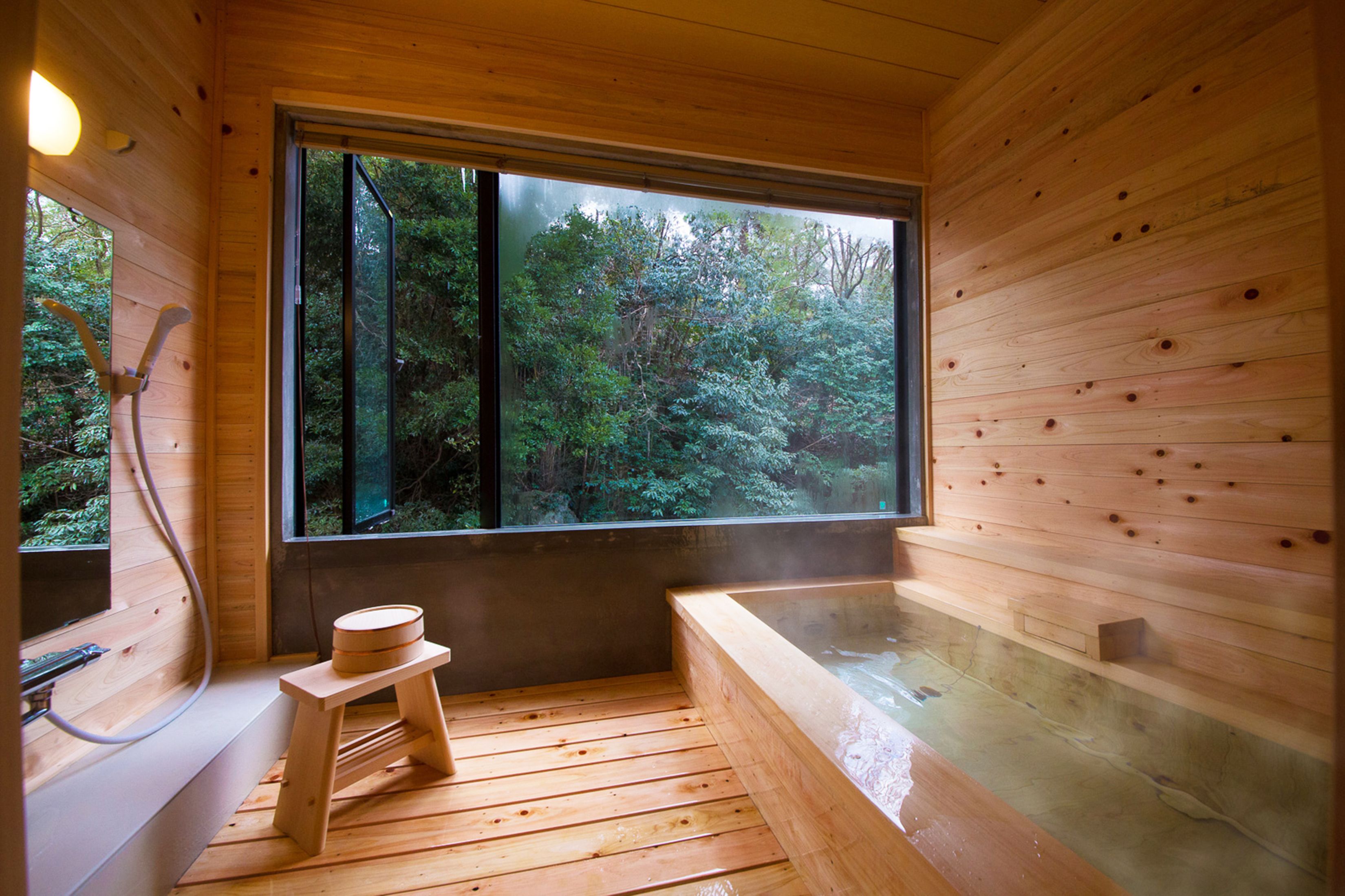 Een houten blokhut met een sauna, een houten bank en een groot raam met uitzicht op een bos.