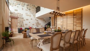Un coin repas avec une table et des chaises en bois, un lustre et un mur en pierre avec un escalier en arrière-plan.