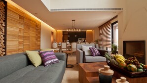 Un salon moderne avec un canapé gris, un lambris en bois, un coin repas avec des chaises et un panier de fruits posé sur une table en bois.