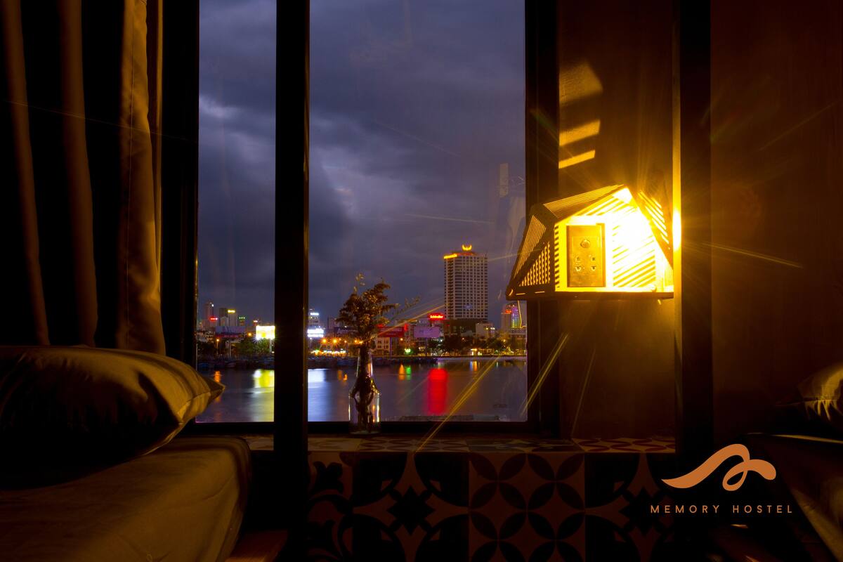A hotel room with a large window overlooking a cityscape at night.