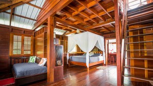 Una habitación de madera con una cama, una cama más pequeña con dosel y una estantería.