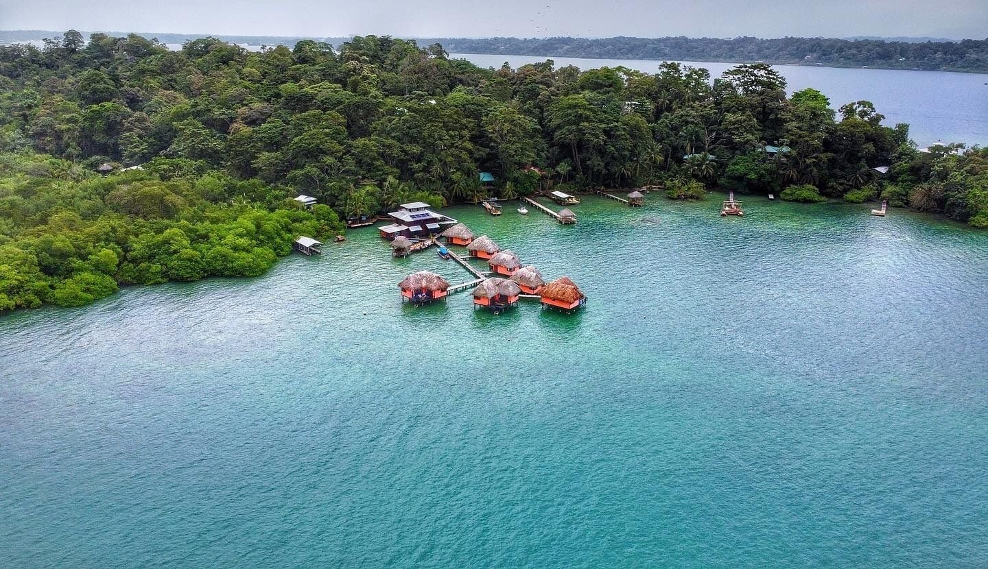 An aerial view of a tropical island with overwater bungalows connected by a dock.
