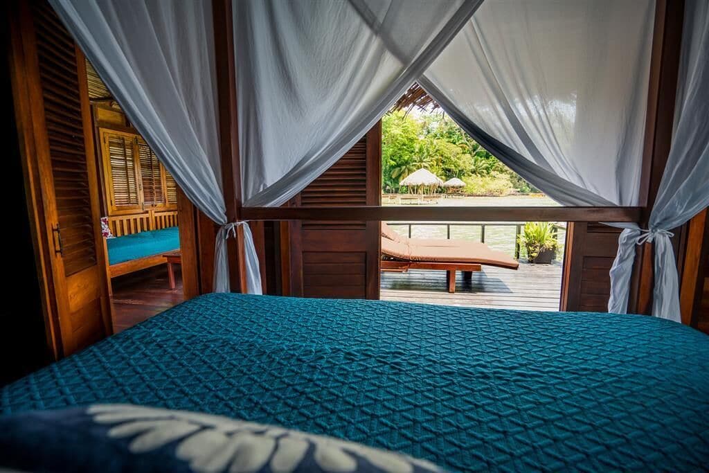 Un dormitorio con cama, cortinas y vista a un espacio exterior con banco y sombrillas.