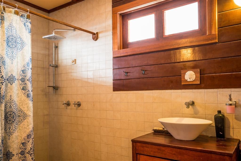 Une salle de bain avec une douche, un lavabo, une horloge et une fenêtre.