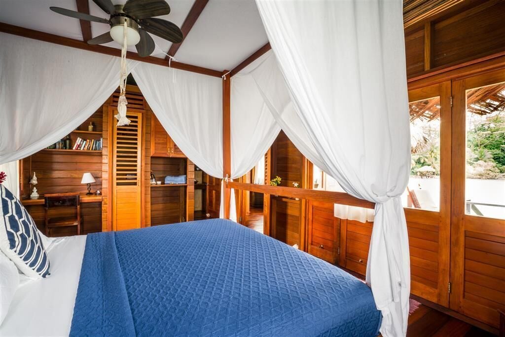 Un dormitorio con una cama, ventilador de techo, paredes de madera y una ventana.