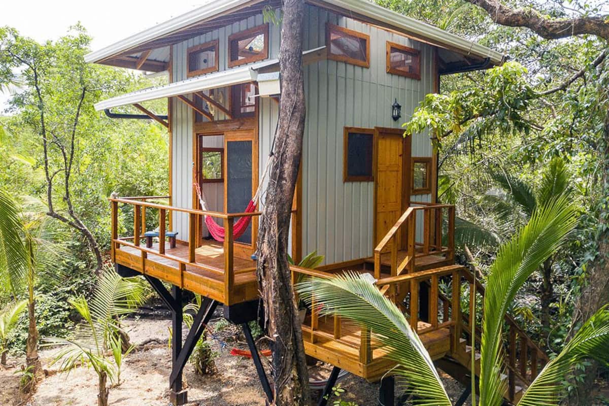 Una cabana de fusta amb un balcó, envoltada de vegetació exuberant.