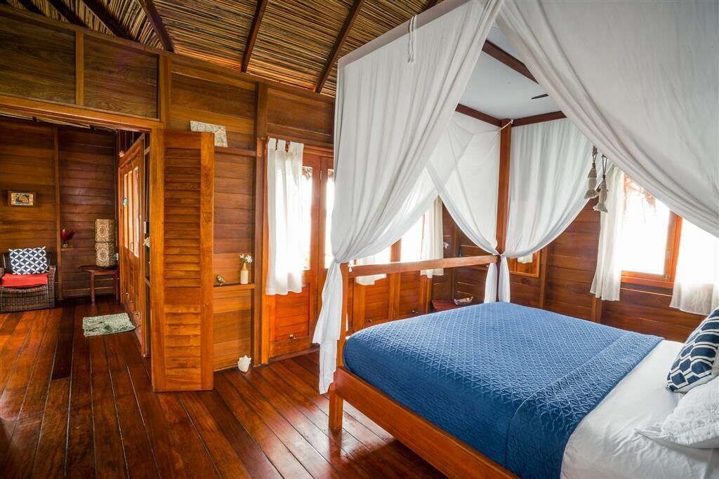 Una habitación de madera con una cama, cortinas blancas y suelo de madera.