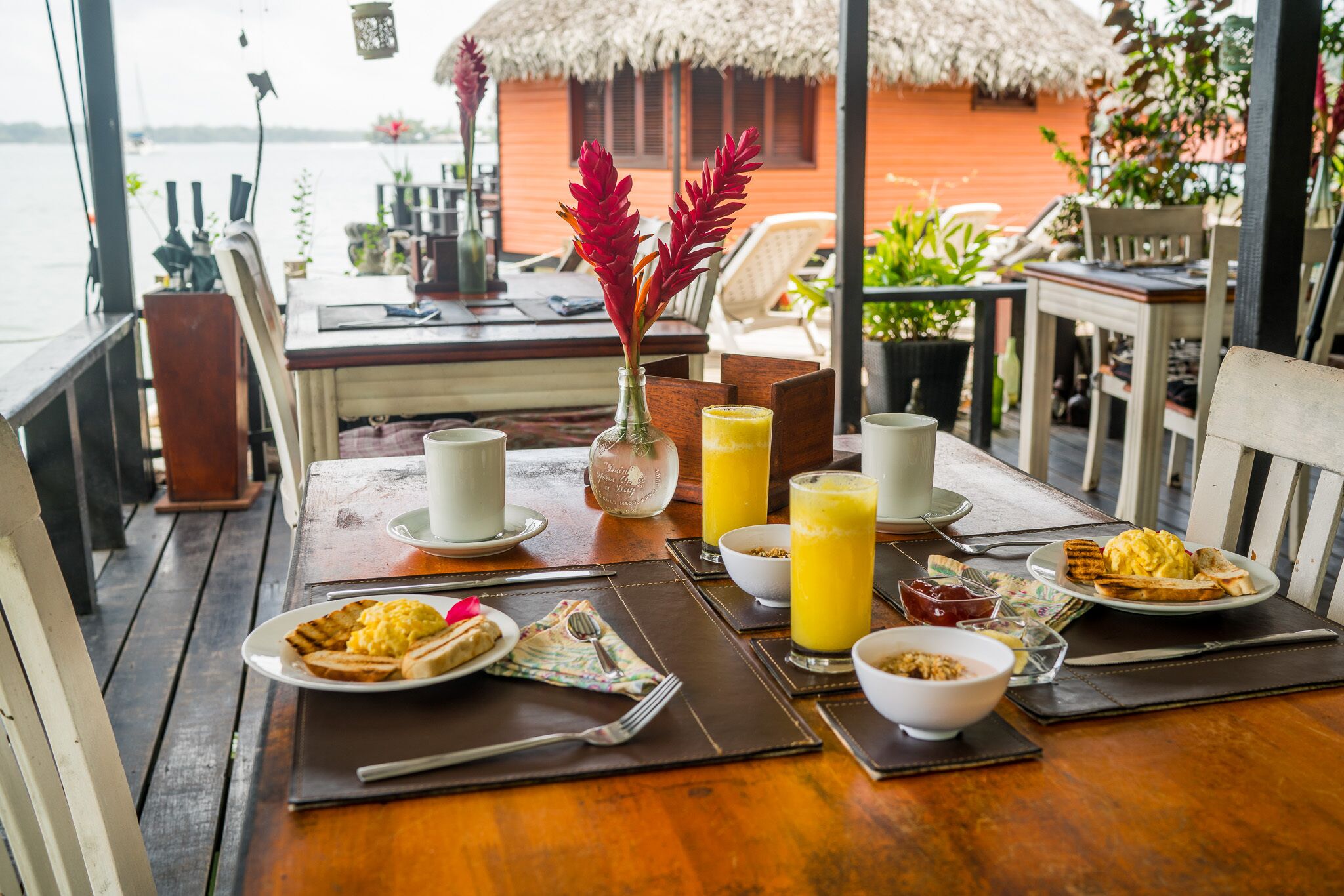 A breakfast table with plates of food, a vase with red flowers, and glasses of orange juice.