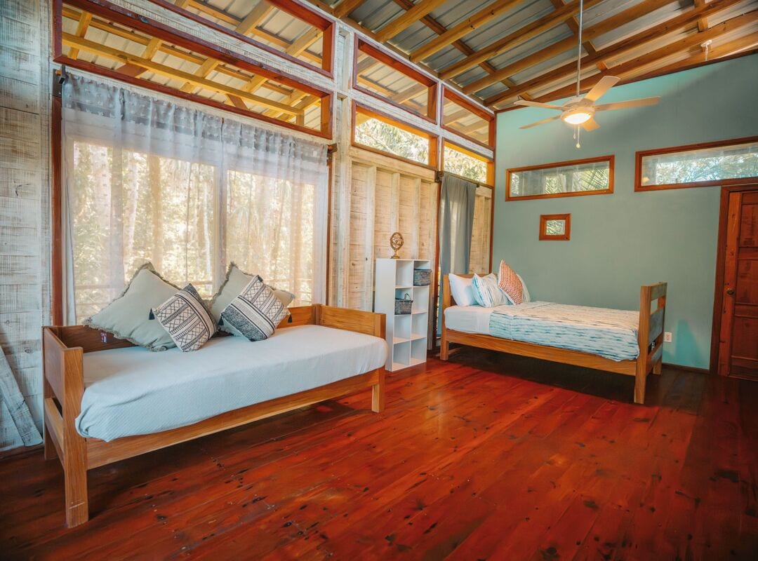A room with two wooden beds, a ceiling fan, and large windows with curtains.