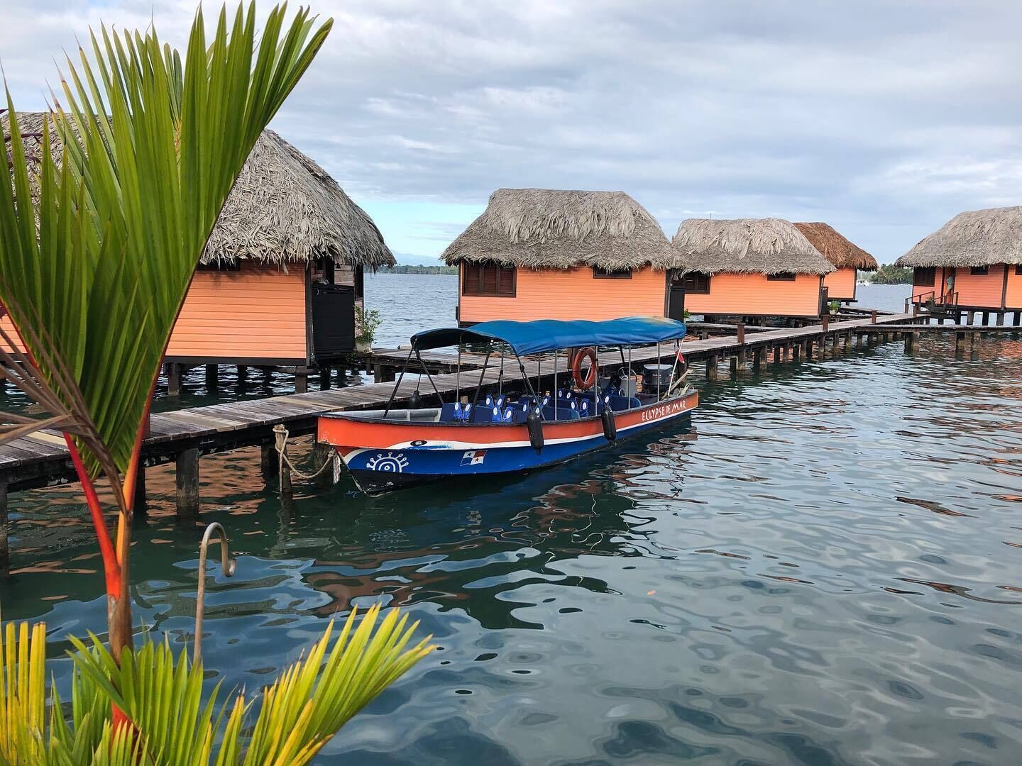 A boat docked at a pier with overwater bungalows in the background.
