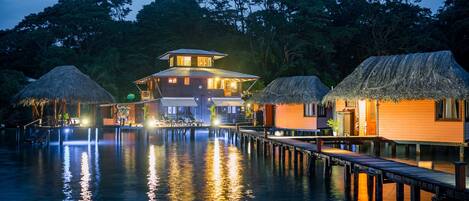 A waterfront property with a central building and two thatched-roof structures connected by a wooden dock.