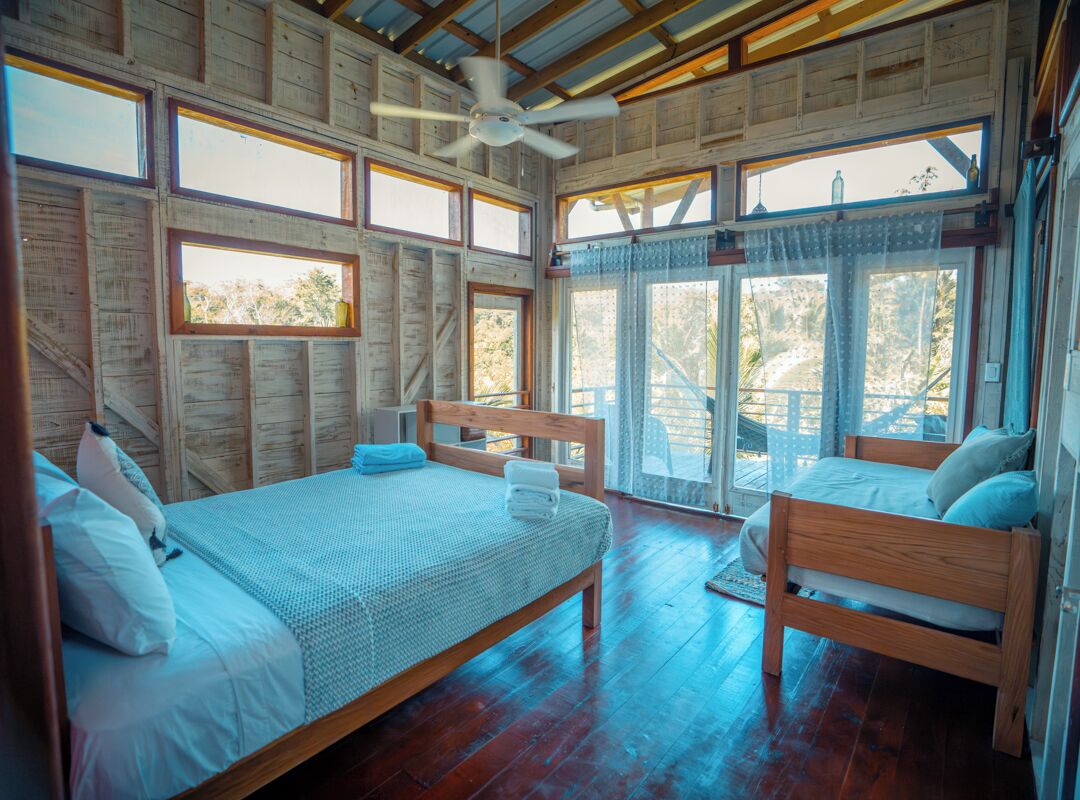 Eine Holzhütte mit zwei Betten aus Holz, einem Deckenventilator und großen Fenstern.