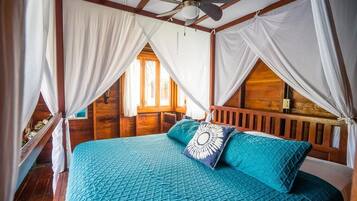 Un dormitorio con techo de madera, una cama con colcha azul, cortinas blancas y un ventilador de techo.