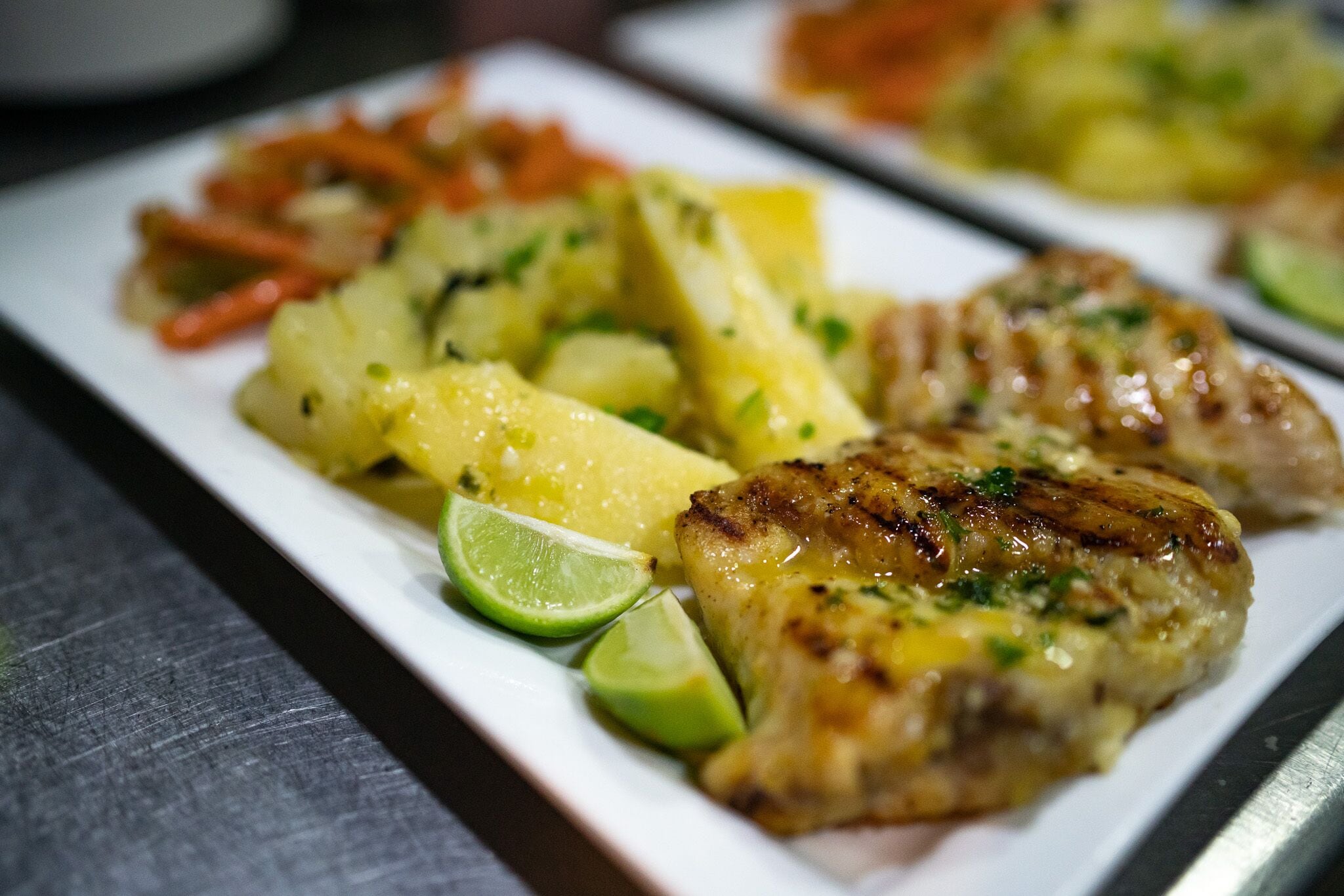 A plate of grilled chicken, pineapple, and carrots with lime wedges.