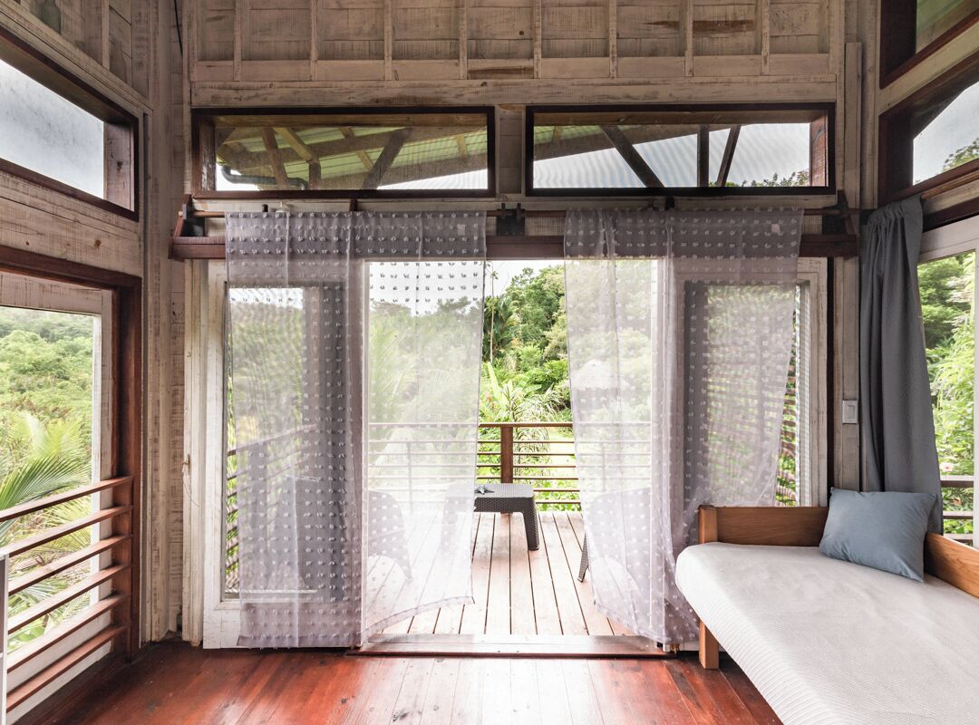 Una habitación con piso de madera, un sofá y vistas a un balcón con una silla.