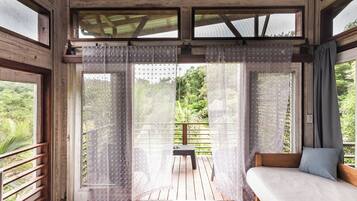 A room with a wooden floor, a sofa, and a view of a balcony with a chair.