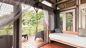 Une terrasse en bois avec un lit et une chaise, une fenêtre avec des rideaux et une vue sur la verdure environnante.