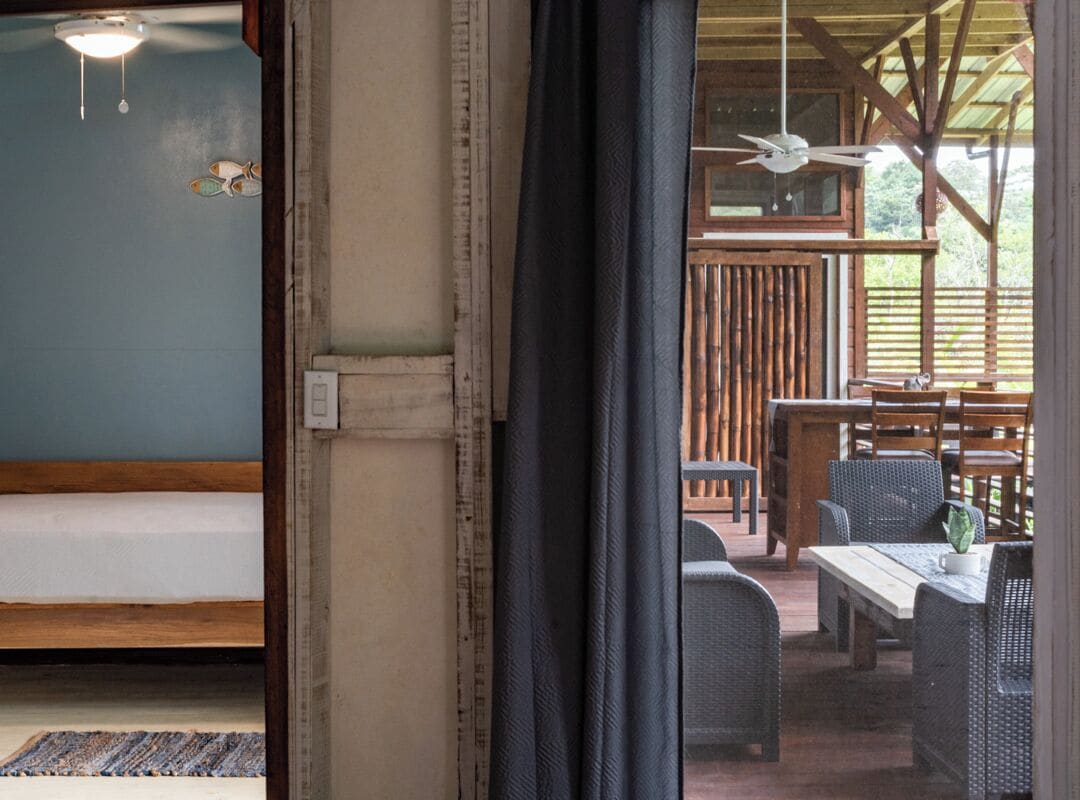 A room with a bed, a window with a view of an outdoor dining area, and a ceiling fan.